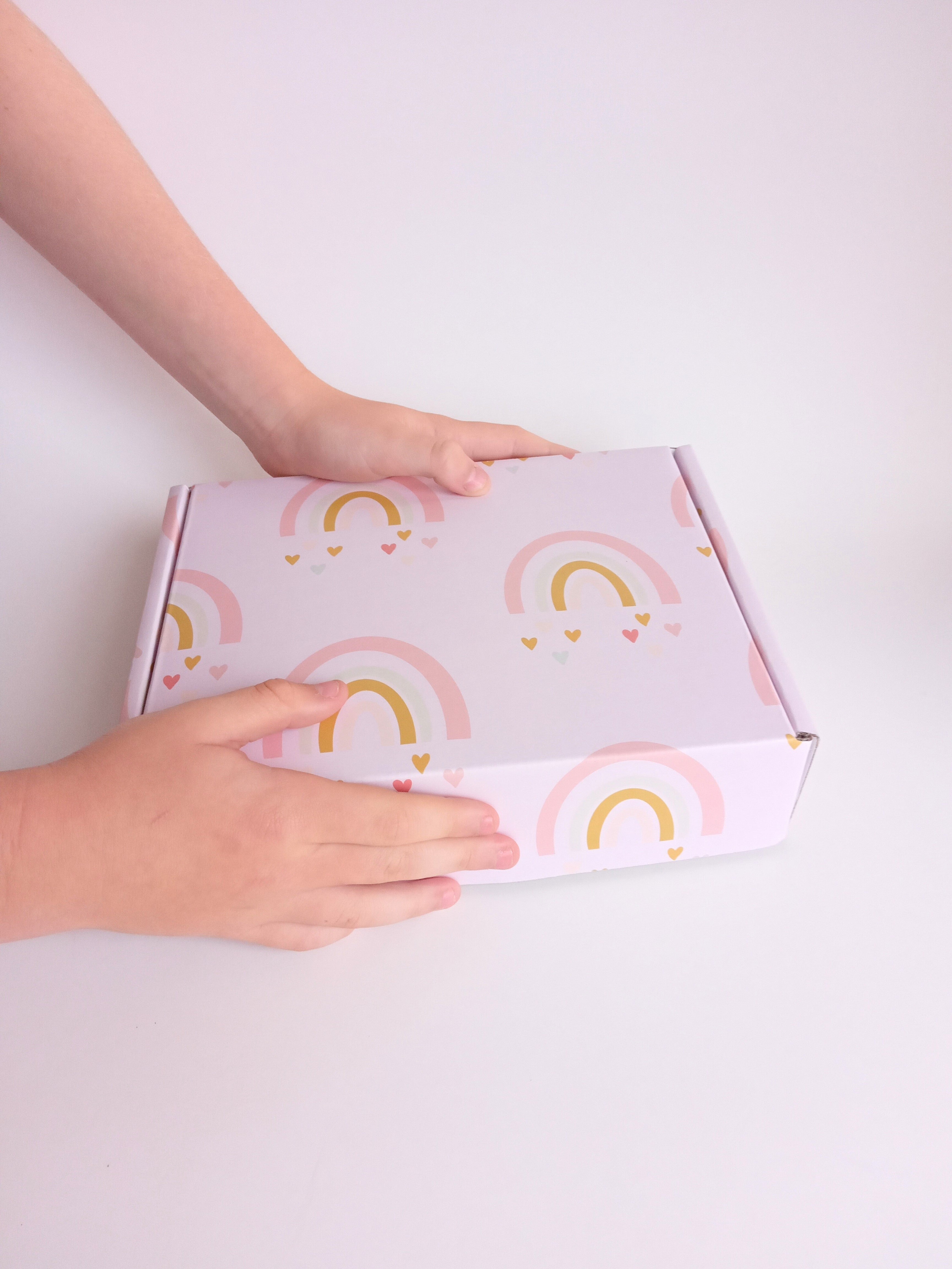 Gift box for kids in a light pink rainbow design, held in kids hands